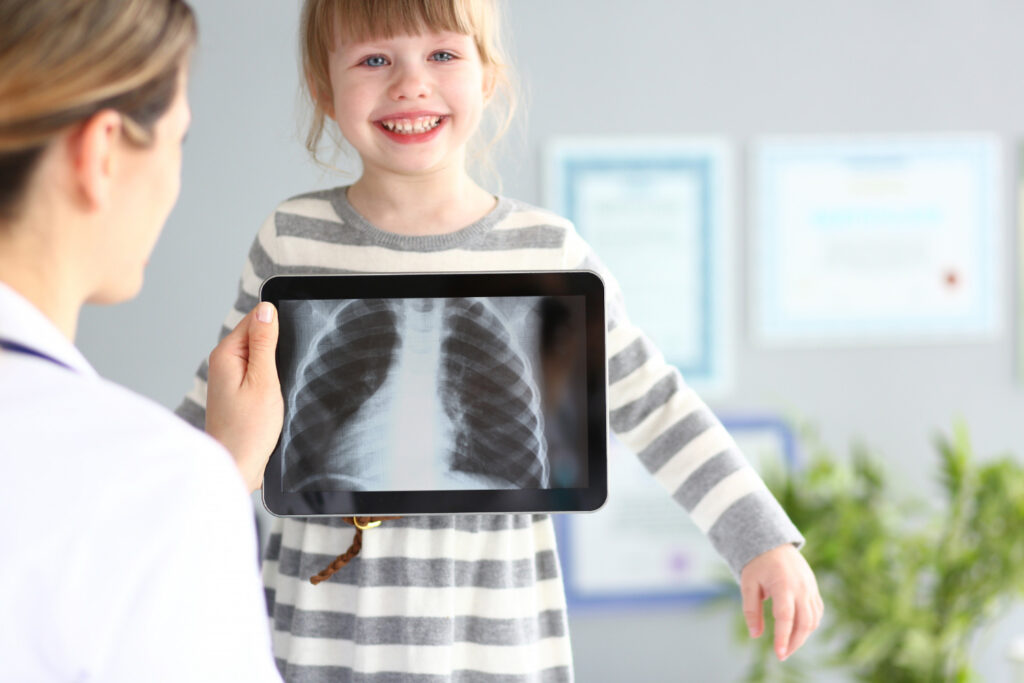 Female doctor showing a smiling child her chest X-ray on a tablet, representing pediatric X-ray examinations