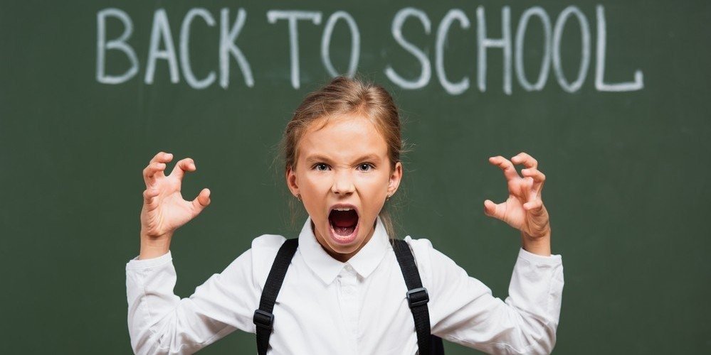 upset girl in front of chalkboard with return to school written on it
