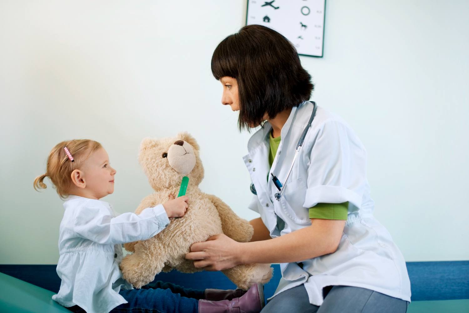A pediatrician and a child each hold one side of a teddy bear during a pediatric urgent care visit.