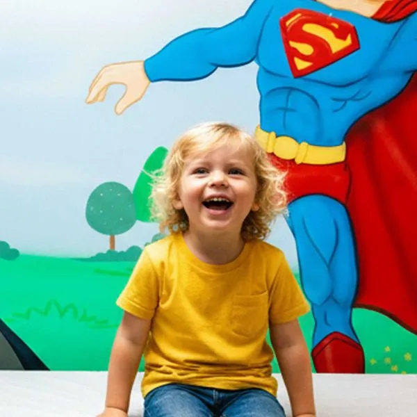Happy child smiling in front of a Superman mural at Just 4 Kids Pediatrics
